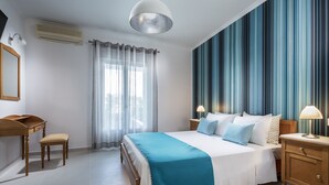 A bedroom with a bed, bedside tables, a desk, and a chair. - Santellini Hotel (Santorini)