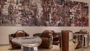 Un intérieur moderne avec des fauteuils en cuir, une table métallique et une grande fresque abstraite sur le mur.