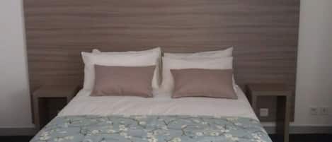 Un lit bien fait, recouvert d’une couvre-lit à motifs floraux et agrémenté de deux oreillers.