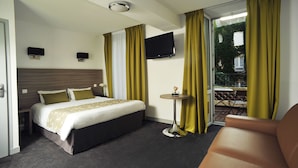 Une chambre d’hôtel avec un lit, une petite table, une télévision et un balcon avec des rideaux jaunes.