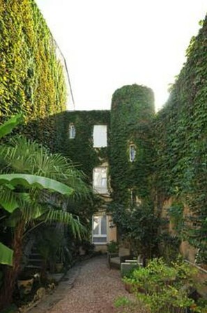 A narrow pathway flanked by buildings covered in ivy, leading to a small window. - Hôtel Atlantic (La Rochelle)