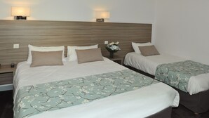 A hotel room with two beds, each with a floral bedspread, a nightstand with a lamp, and a vase with flowers.