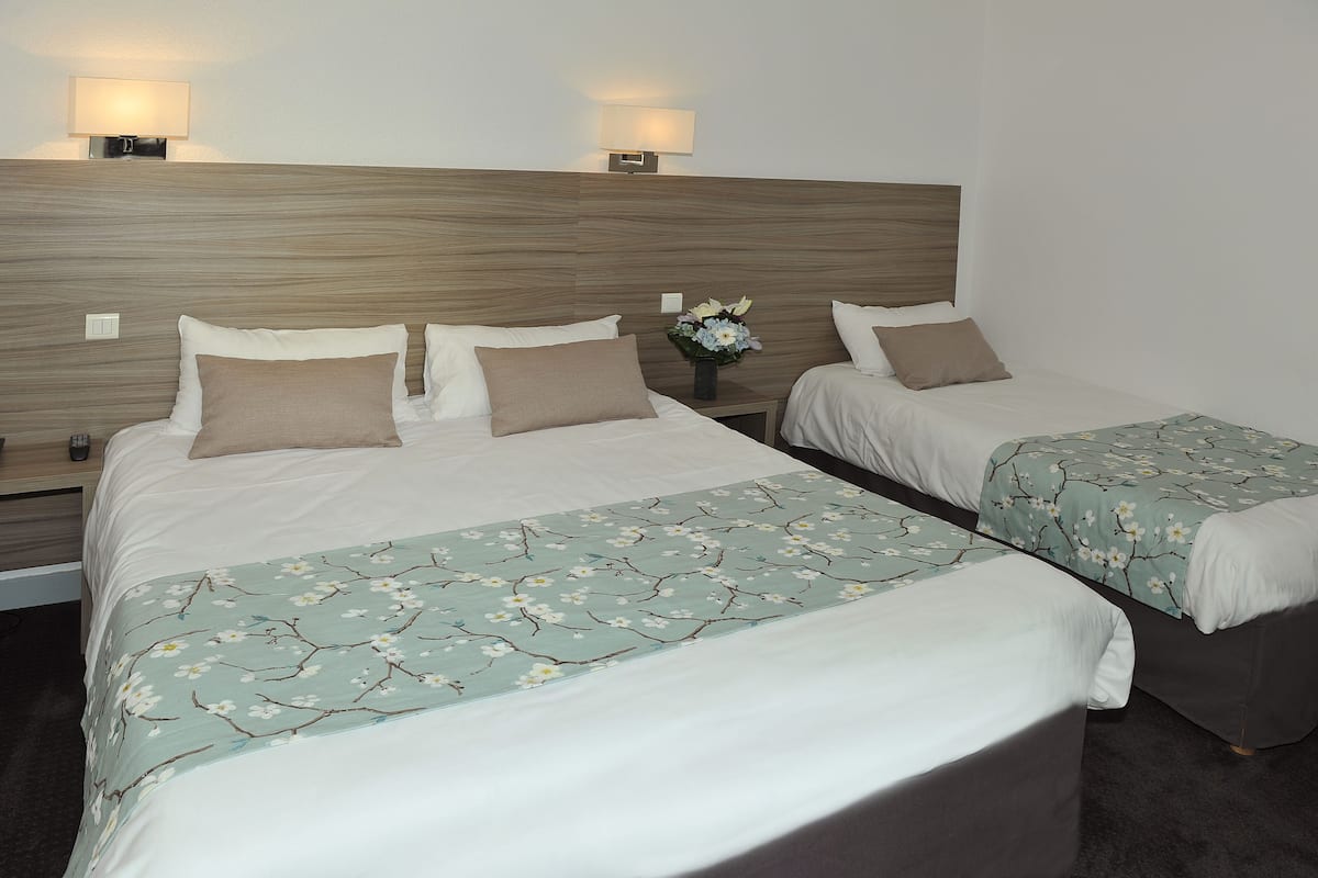 Habitació d'hotel amb dos llits, cadascun amb un llençol floral, una tauleta de nit amb una làmpada i un vas amb flors.