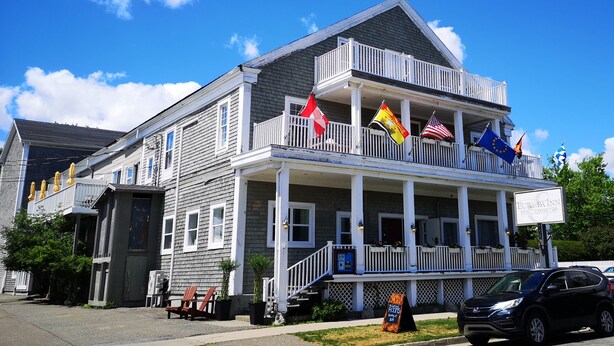 A two-story building with a balcony, multiple flags, and a sign indicating it is a hotel and coffee shop. - Europa Inn (St. Andrews)