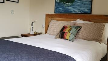 A neatly made bed with a blue quilt, a wooden headboard, and a colorful pillow.