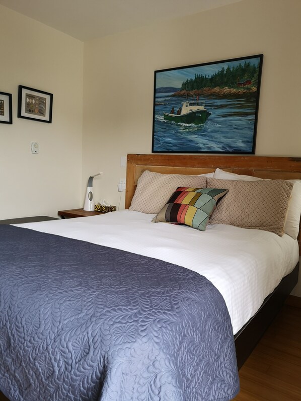 A neatly made bed with a blue quilt, a wooden headboard, and a colorful pillow.