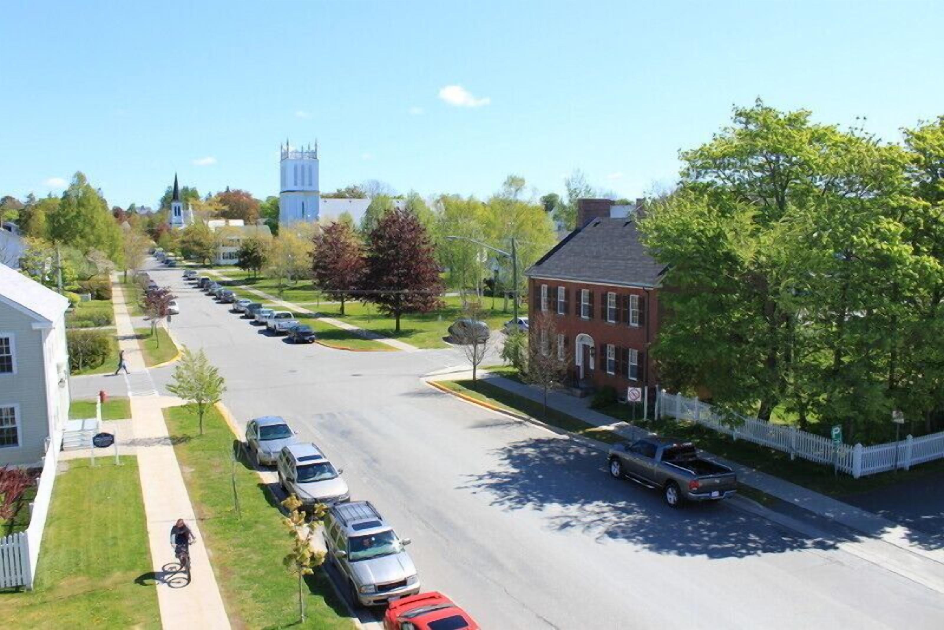 A street view with parked cars, a cyclist, and a church in the background.