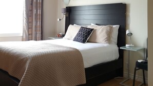A modern bedroom with a large bed, a headboard, a bedside table with a lamp, and two wall-mounted artworks. - Europa Inn (St. Andrews)