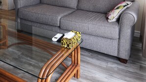 A grey sofa with a cushion, a glass coffee table, and a painting of a landscape on the wall. - Europa Inn (St. Andrews)