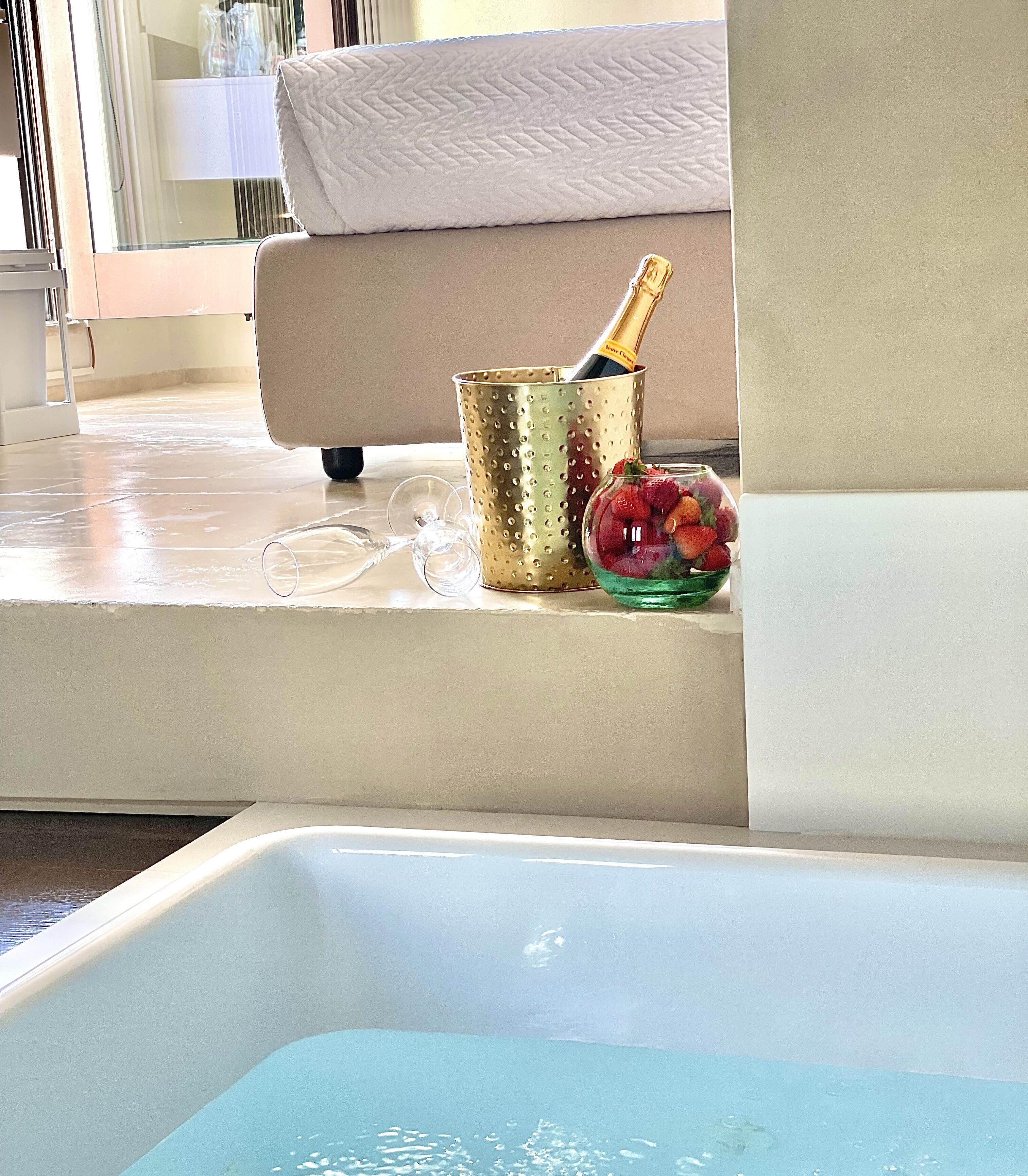 Una bañera con un vaso de agua, un cubo dorado con una botella y un cuenco de fresas.