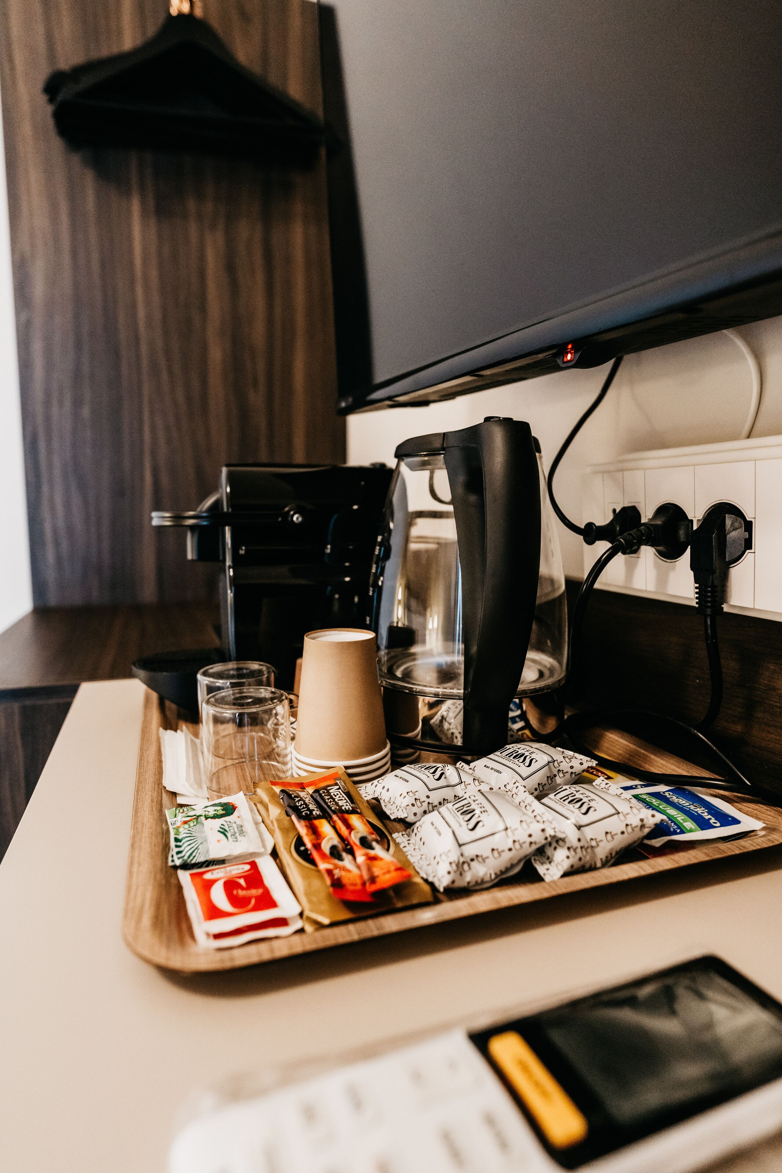 Eine Küchenarbeitsplatte mit einer Kaffeemaschine, einem Glas, einer Tasse und einer Tablett mit Kaffee-Kapseln und Zuckerportionen.