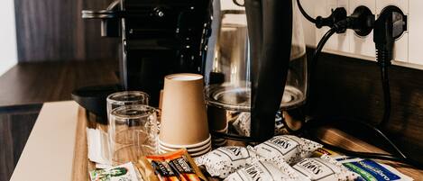 Eine Küchenarbeitsplatte mit einer Kaffeemaschine, einem Glas, einer Tasse und einer Tablett mit Kaffee-Kapseln und Zuckerportionen.