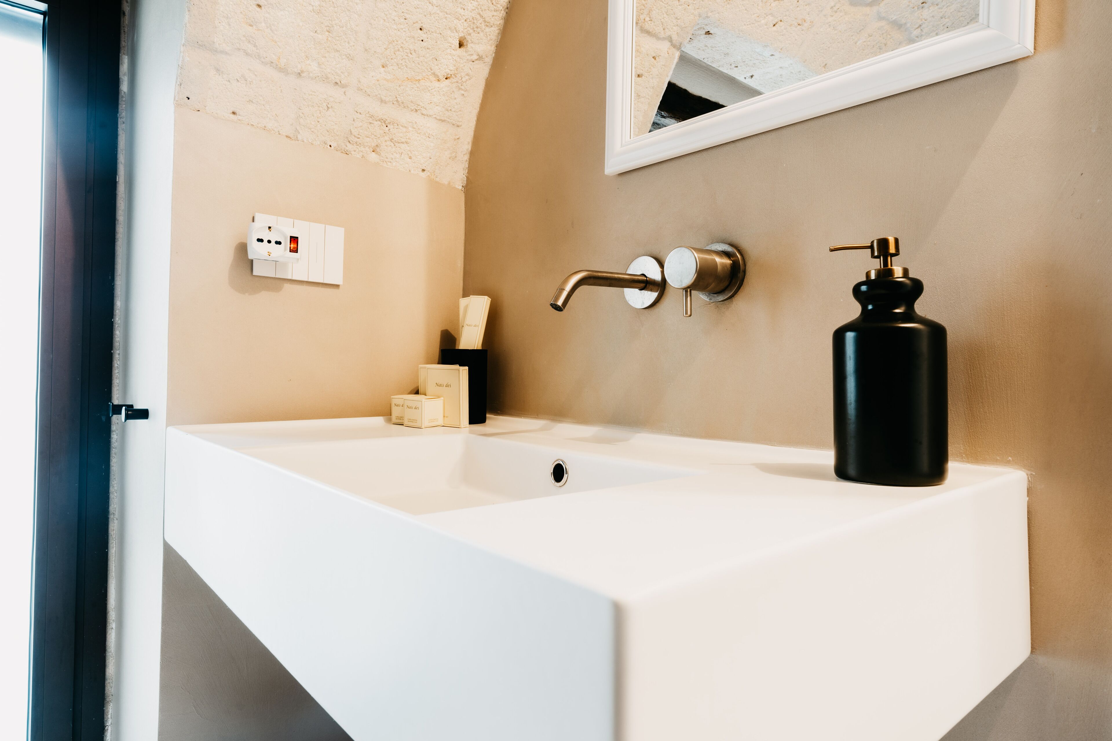 Een badkamer met een witte wastafel, een kraan, een zeepdispenser en een spiegel aan de muur.