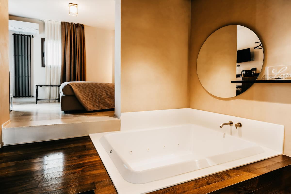 A modern bathroom with a large bathtub, a round mirror, and a wooden vanity.