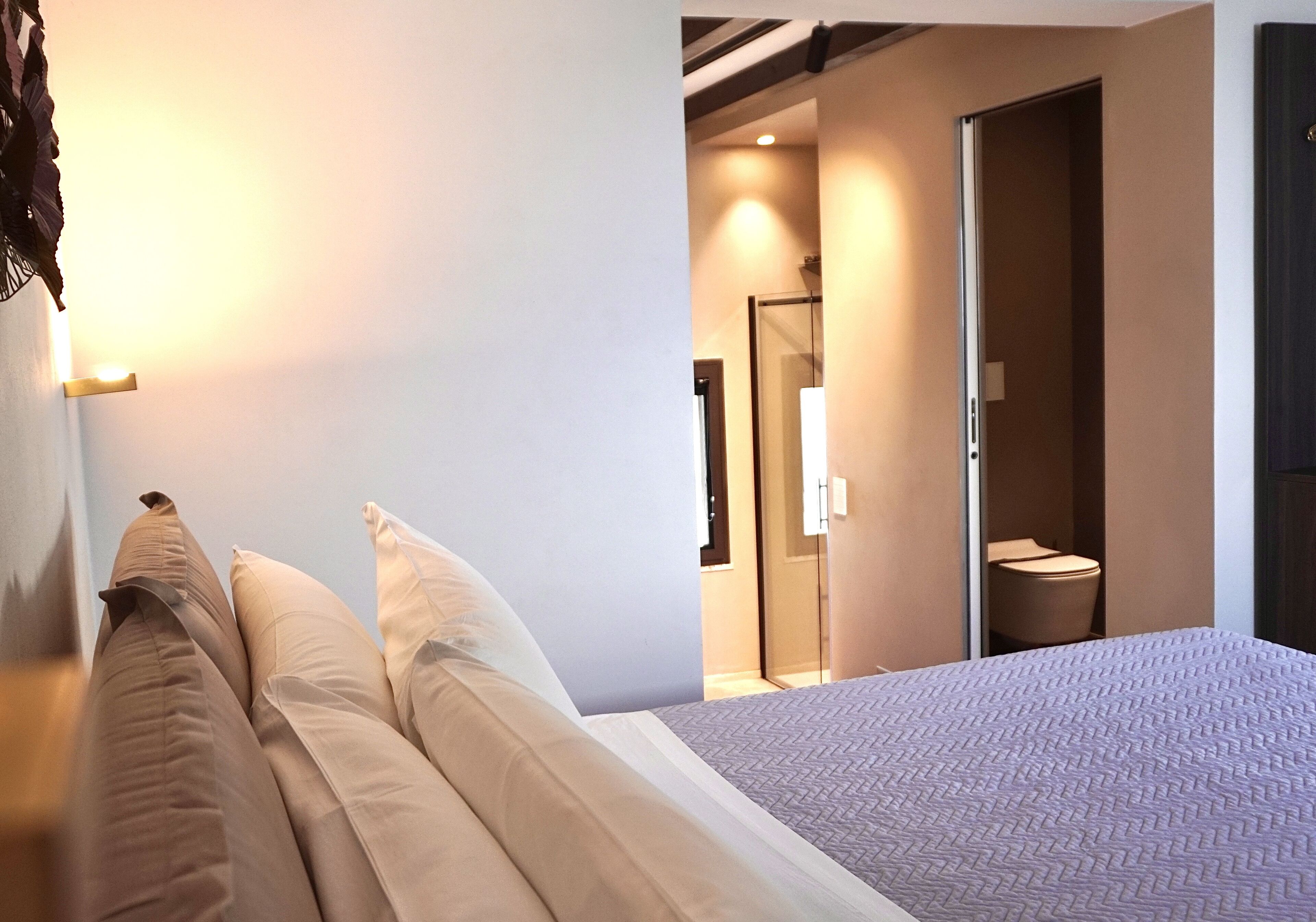 Ein modernes Hotelzimmer mit einem großen Bett, einem Badezimmer mit Glastür und einer sichtbaren Duschkabine.