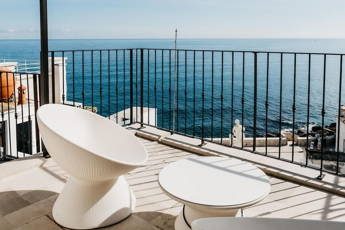 A balcony with a white bathtub, a round table, and a view of the sea.