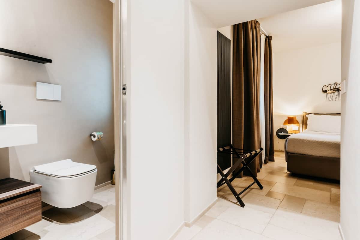 A modern hotel room with a toilet, sink, and a bed.