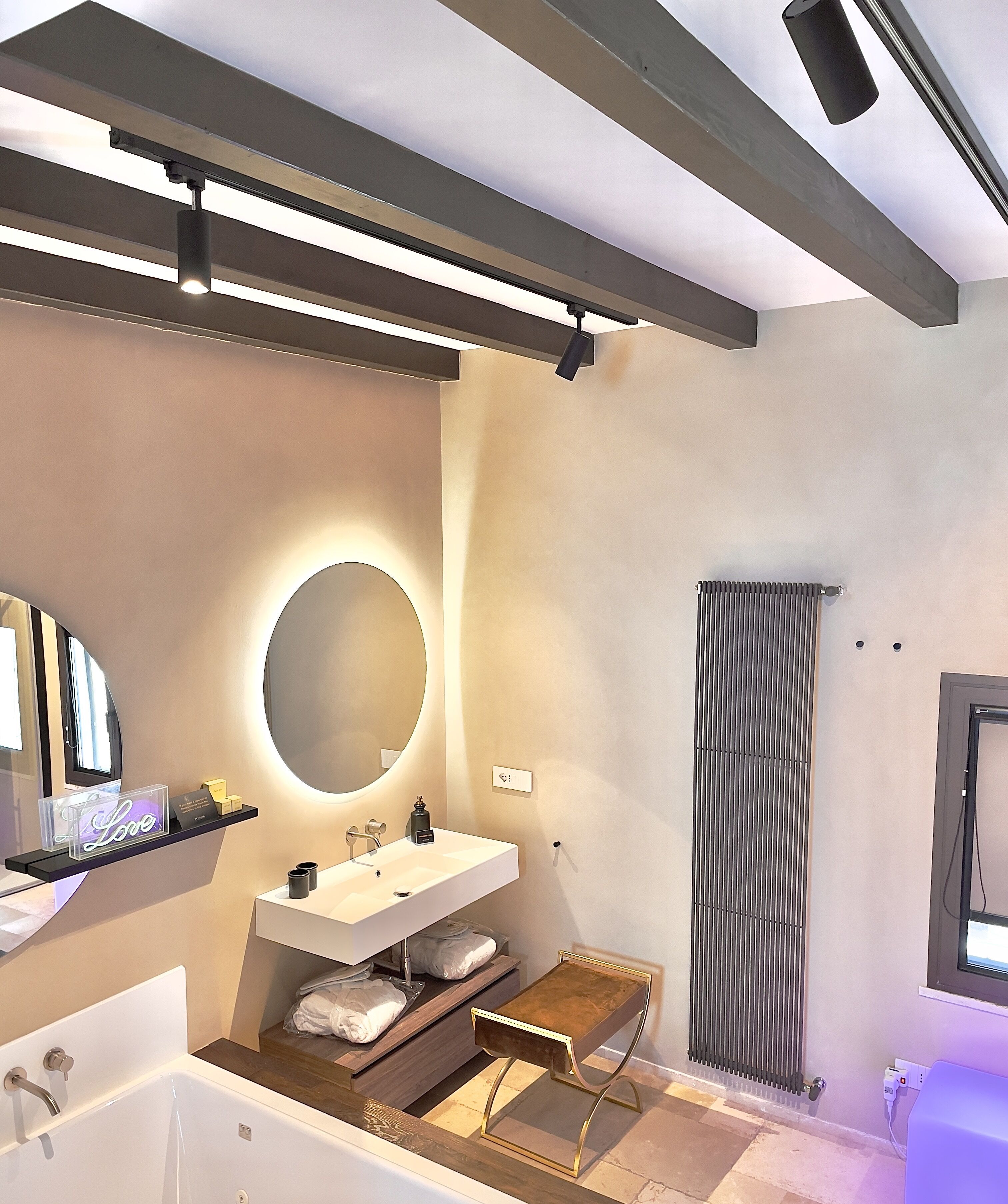 Un baño moderno con una bañera grande, un espejo redondo, un lavamanos blanco y un estante con artículos de aseo.