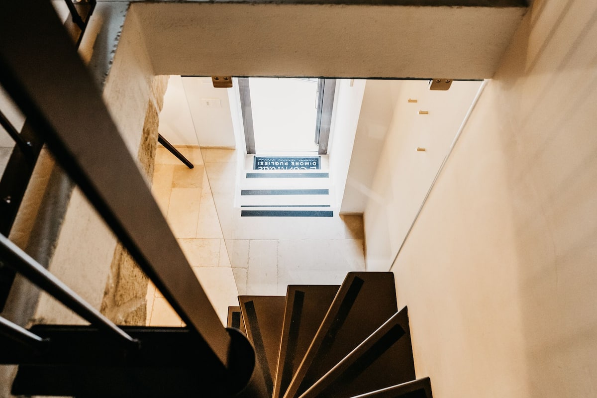 A spiral staircase with a metal railing, leading to a landing with a sign that reads "Original."