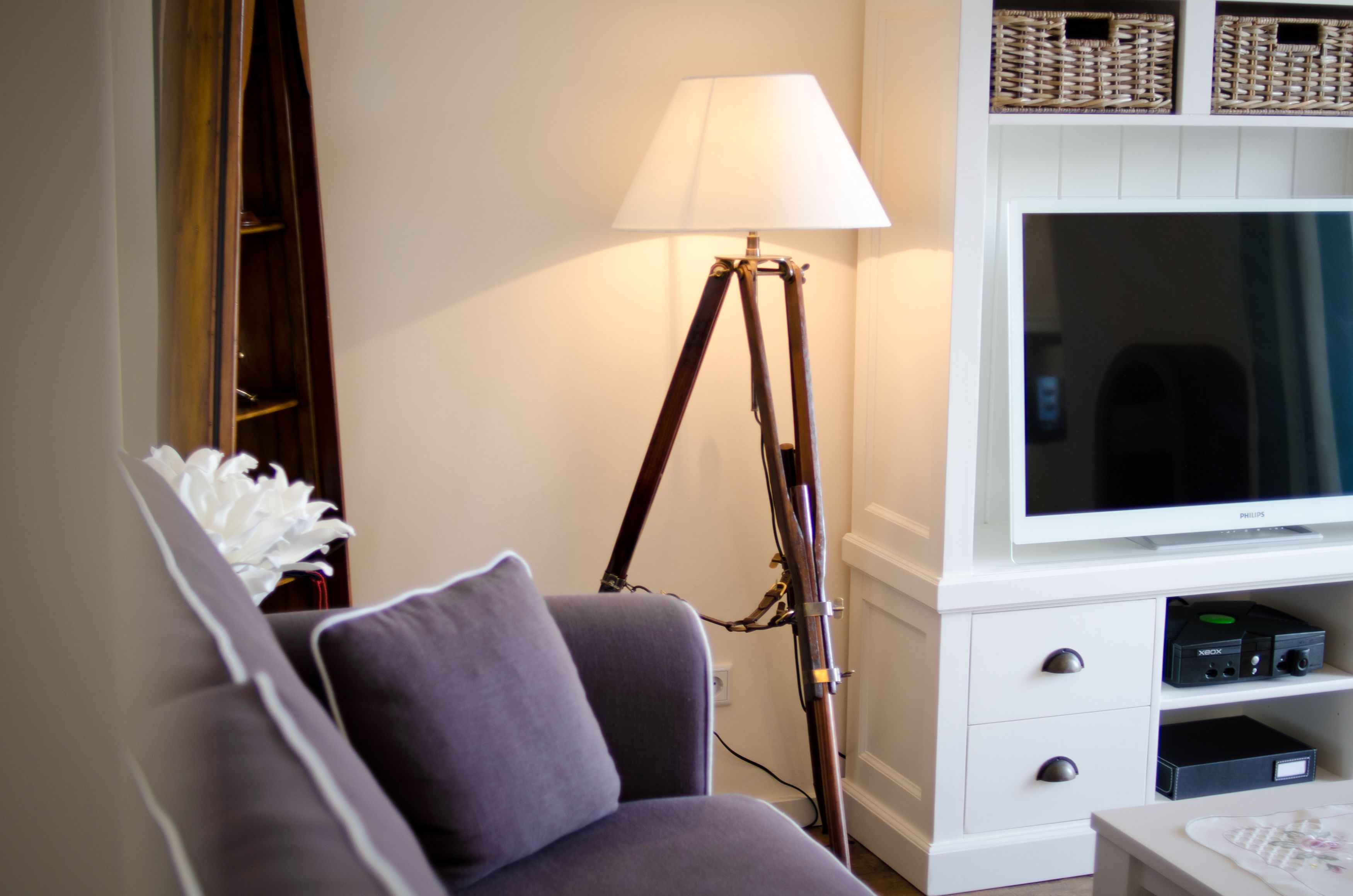 A living room with a sofa, a floor lamp, a flat-screen TV, and a cabinet with electronic devices.