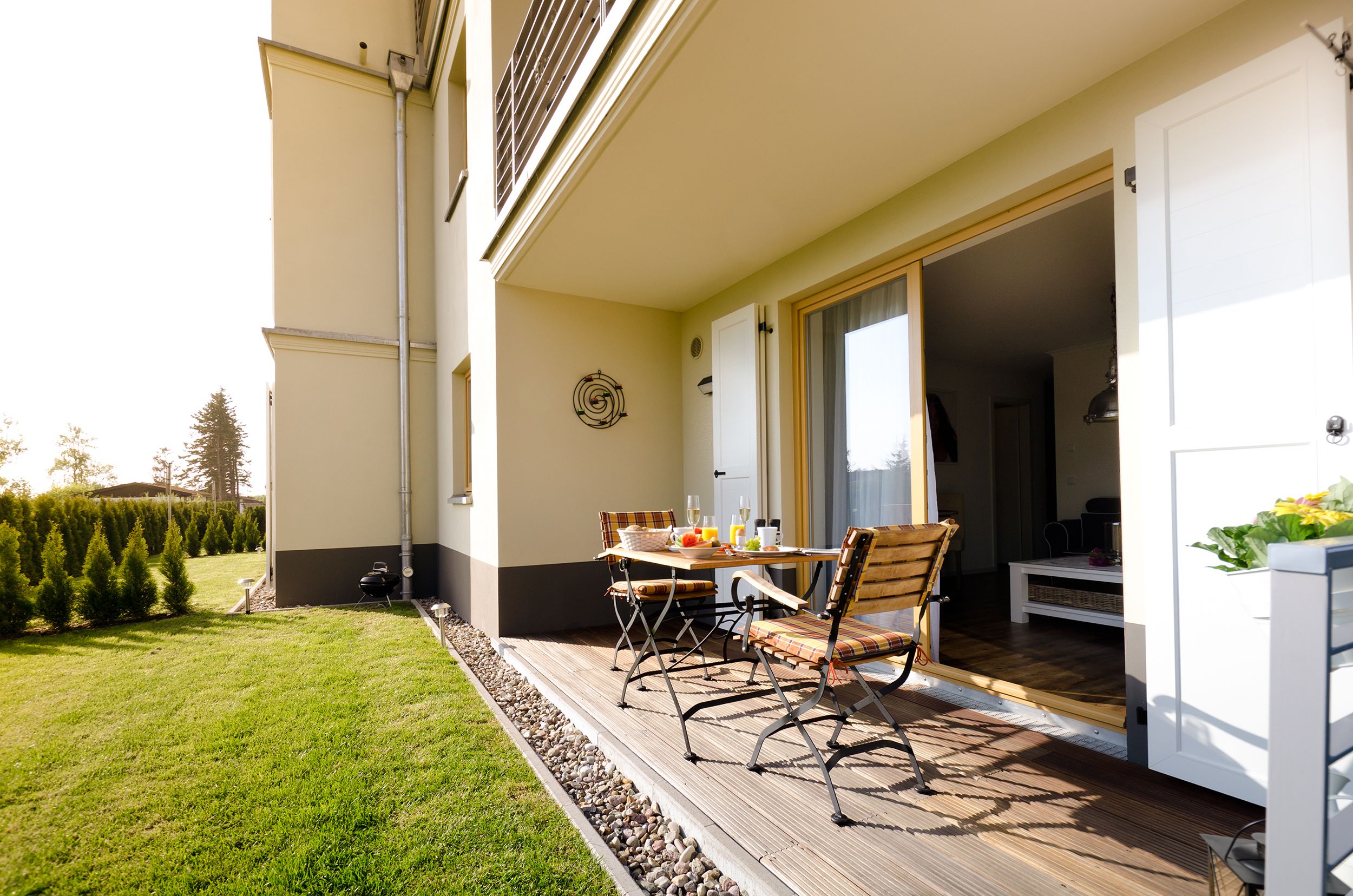 An outdoor patio with a table and chairs, a white door leading to an interior space, and a well-maintained lawn.