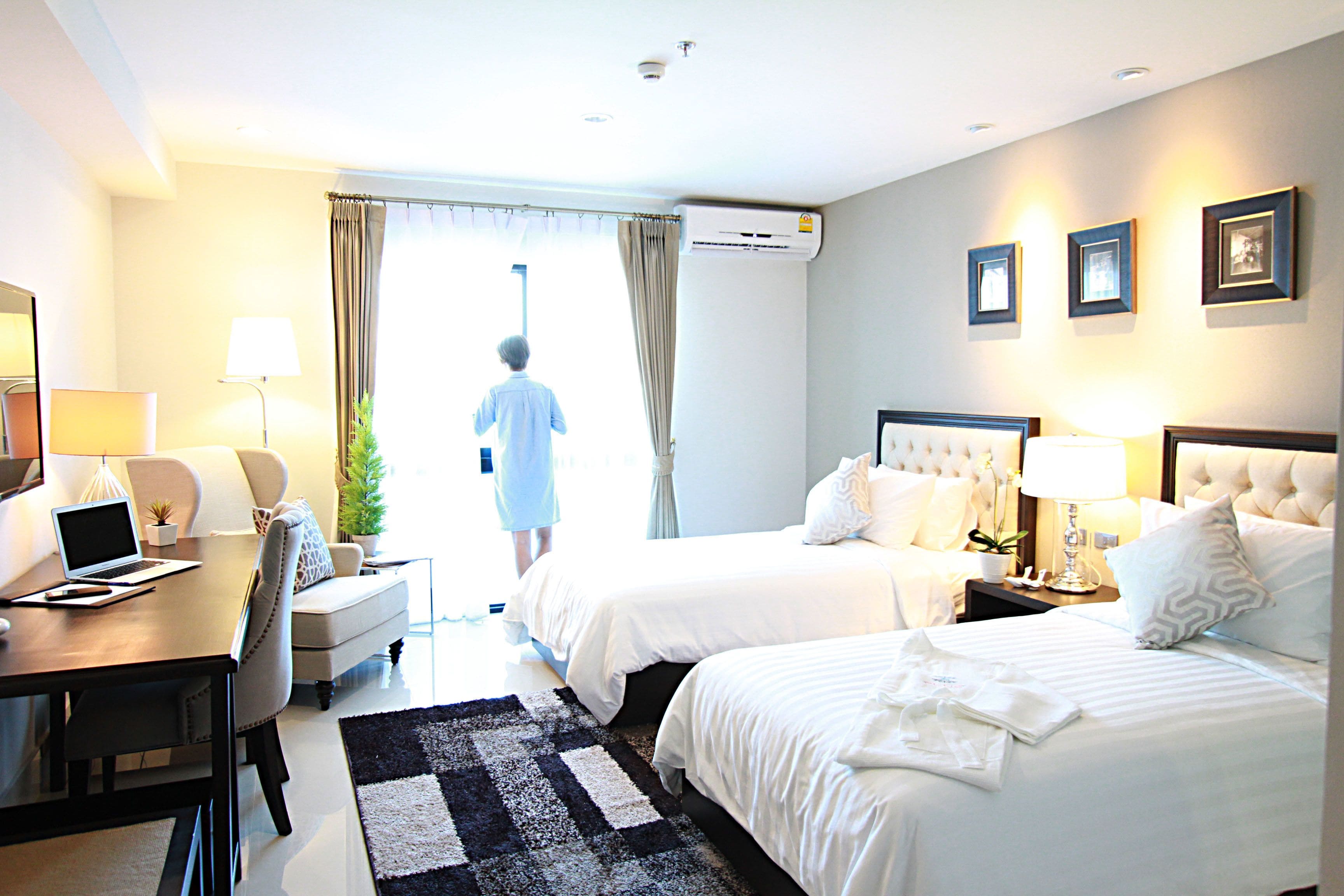 A hotel room with two beds, a desk with a laptop, a chair, a coffee table, and a dining table.