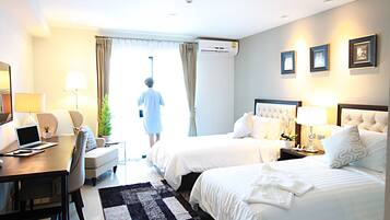 A hotel room with two beds, a desk with a laptop, a chair, a coffee table, and a dining table.