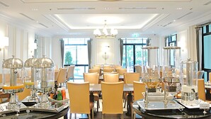 A hotel dining area with round tables, chairs, and a chandelier. - SN Plus Hotel - SHA Plus (Pattaya)