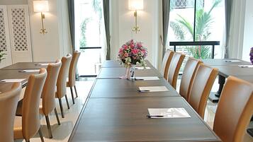 A conference room with a long table, chairs, a vase of flowers, and two wall-mounted lamps.