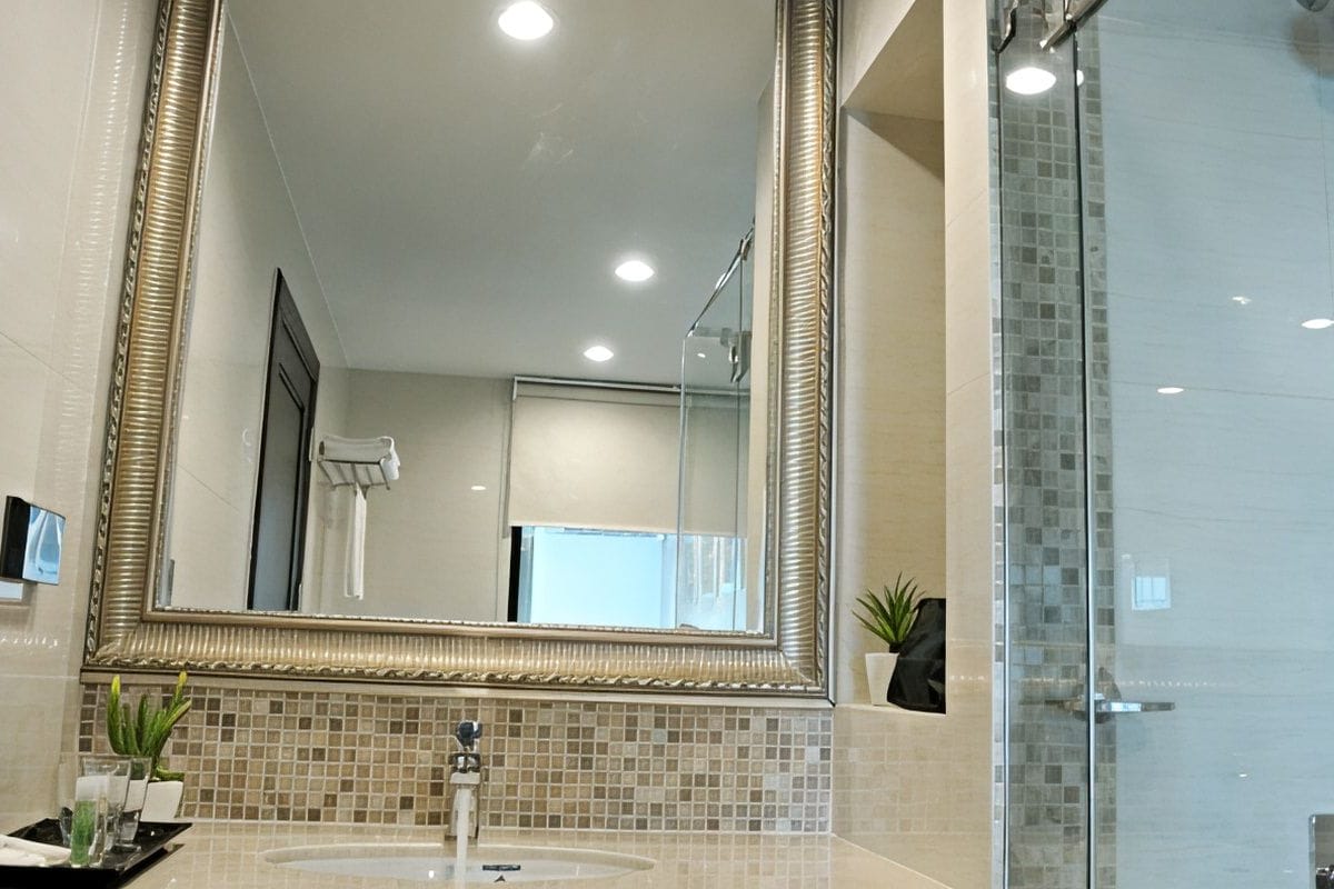 A modern bathroom with a large mirror, a glass shower enclosure, and a sink with a tray of toiletries.