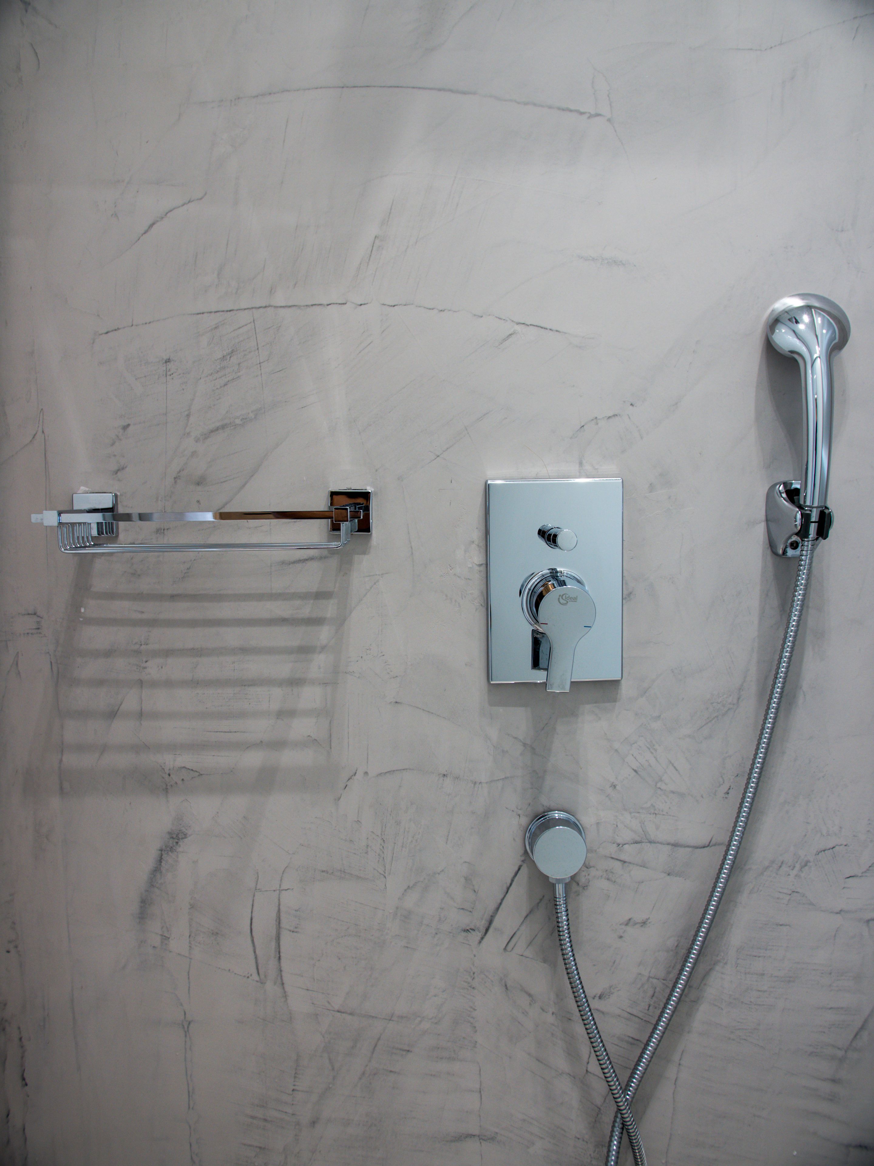 A bathroom with a wall-mounted towel rack, a handheld showerhead, and a control panel.