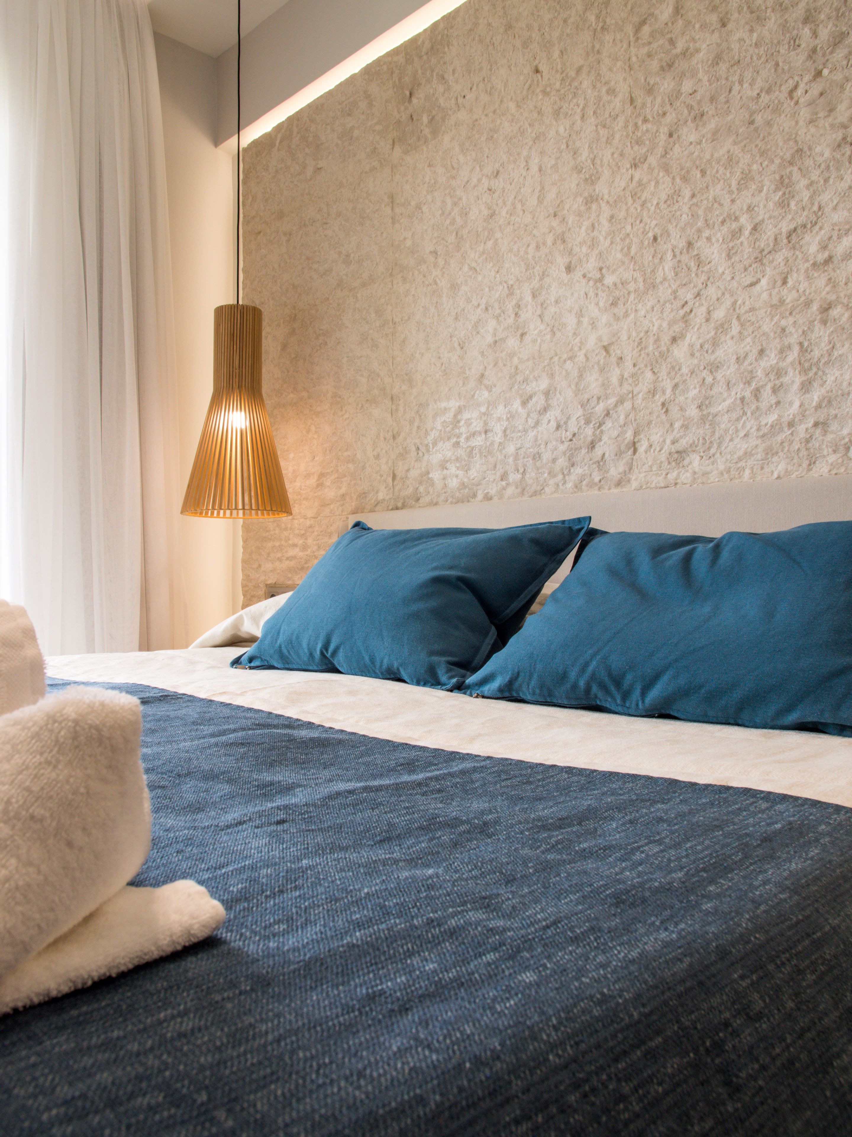A modern hotel room with a large bed, a textured wall, and a hanging pendant light.