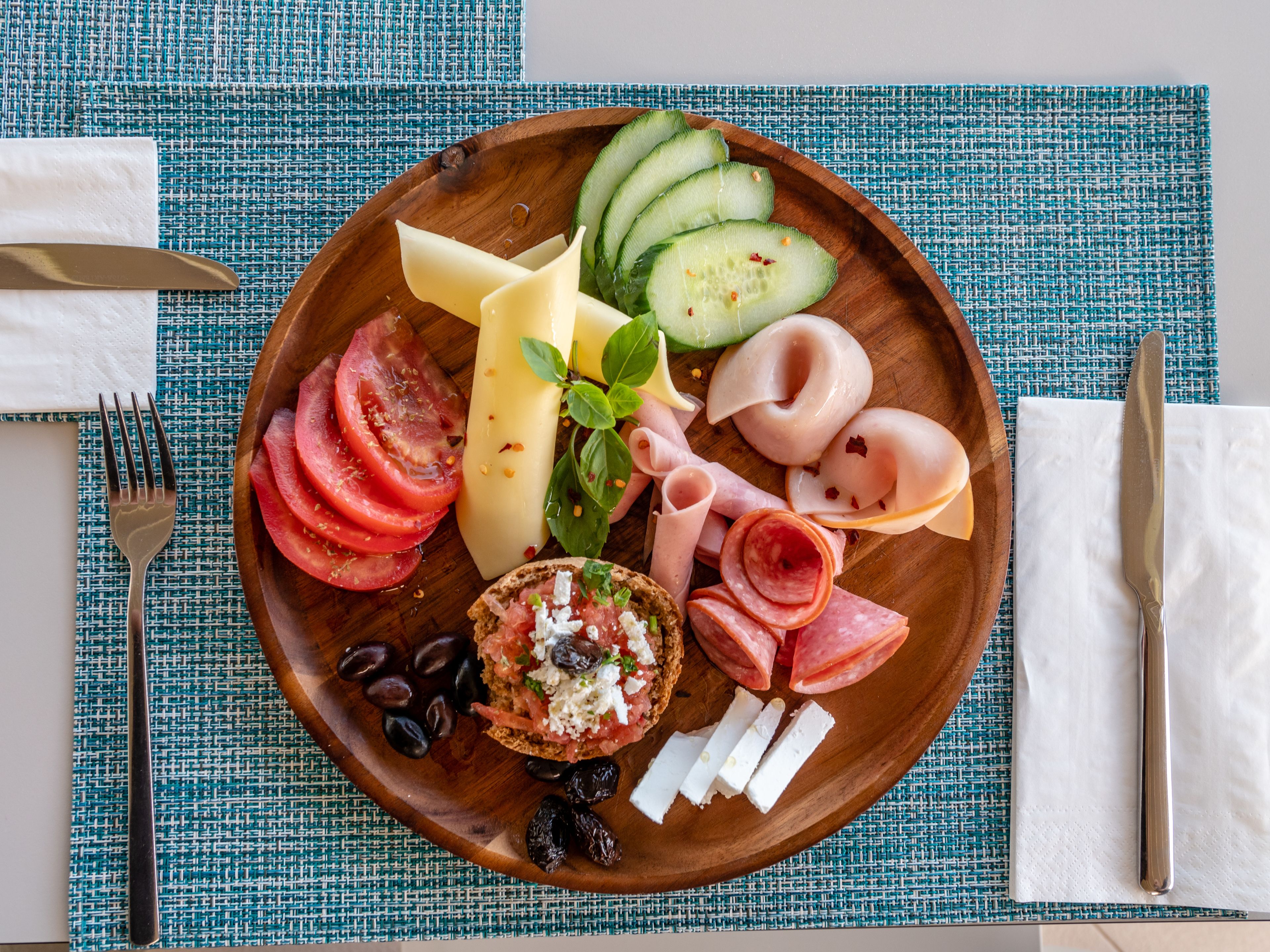 Una tabla de madera con rodajas de tomate, pepino, queso, aceitunas y diferentes tipos de carne.