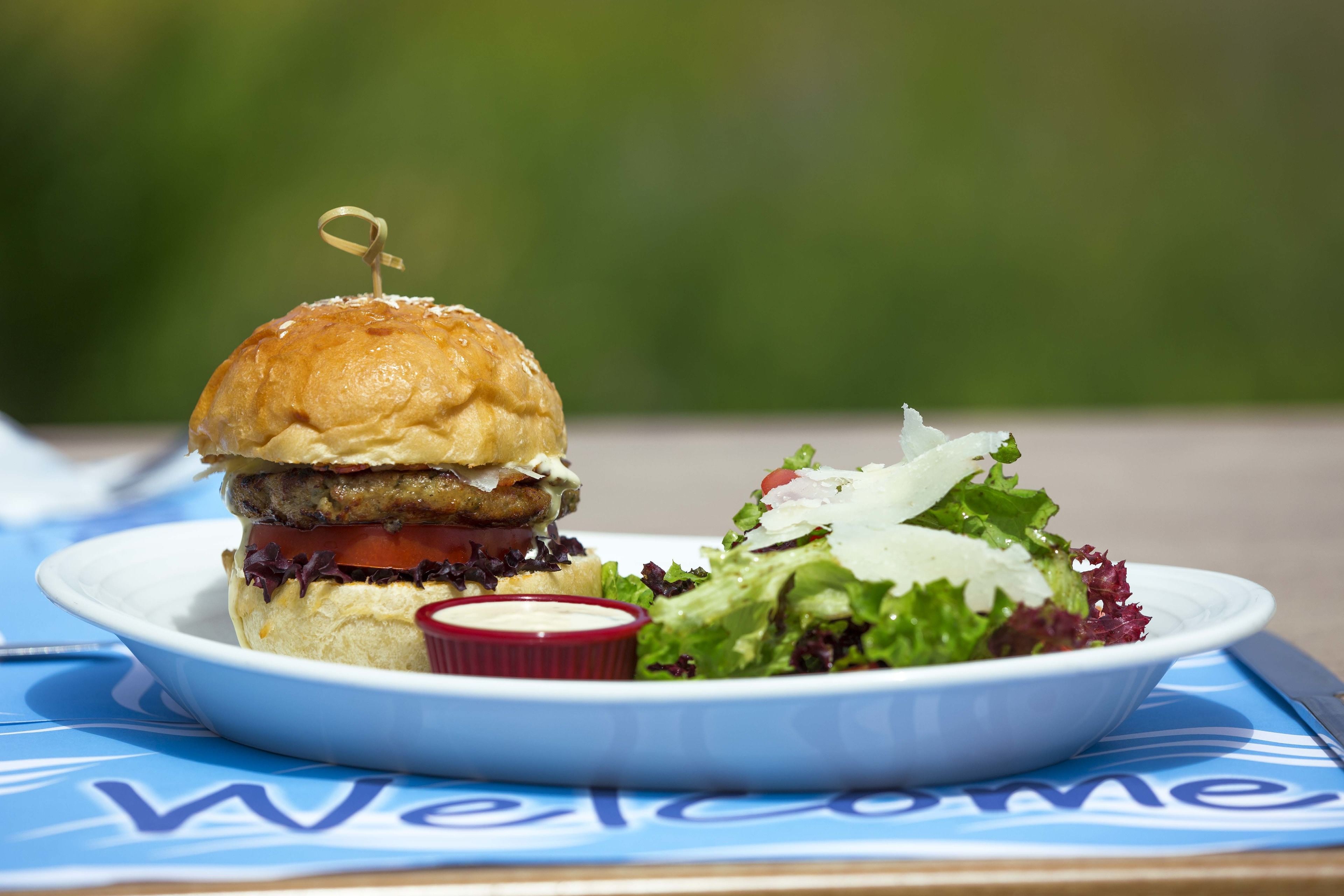 En tallerken med burger og salat på et bord med en velkomstserviet.