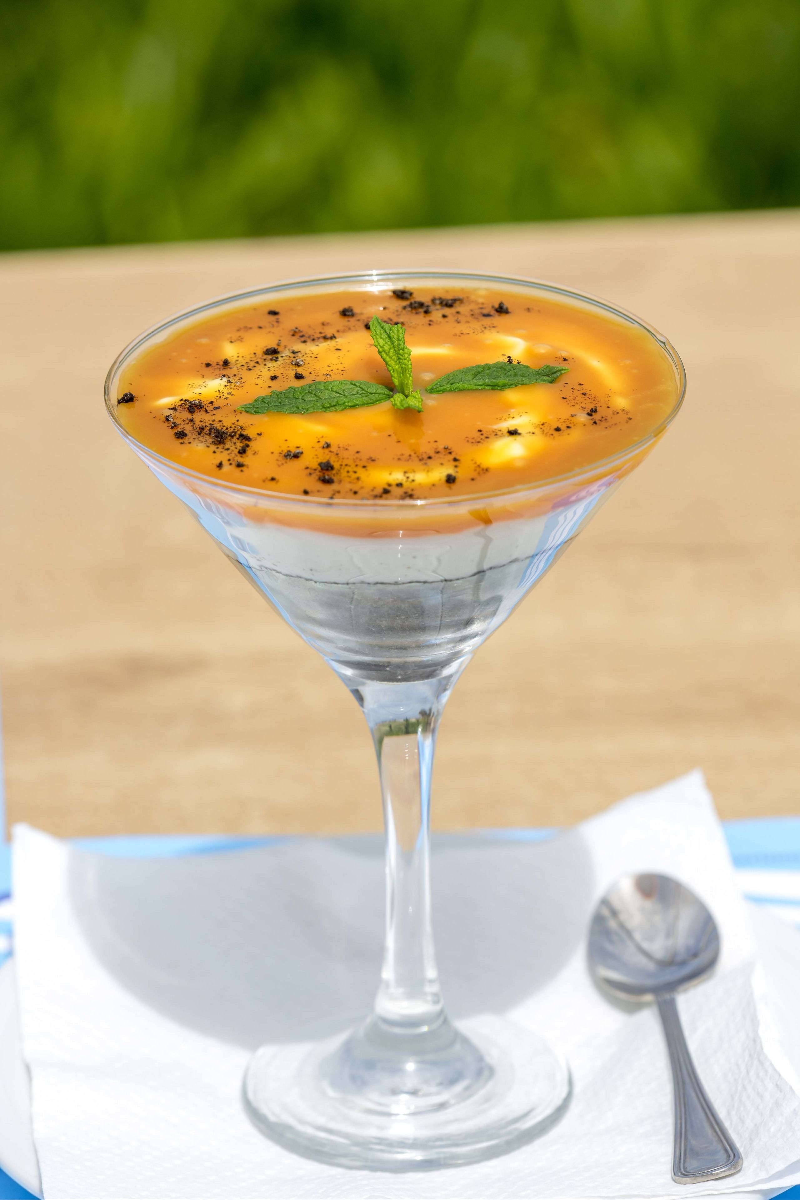 A cocktail in a martini glass with a mint garnish, served on a white napkin with a spoon beside it.