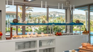 Un buffet disposé de manière attrayante, avec vue sur une piscine et des palmiers, agrémenté d’une nappe bleue et de divers plats.