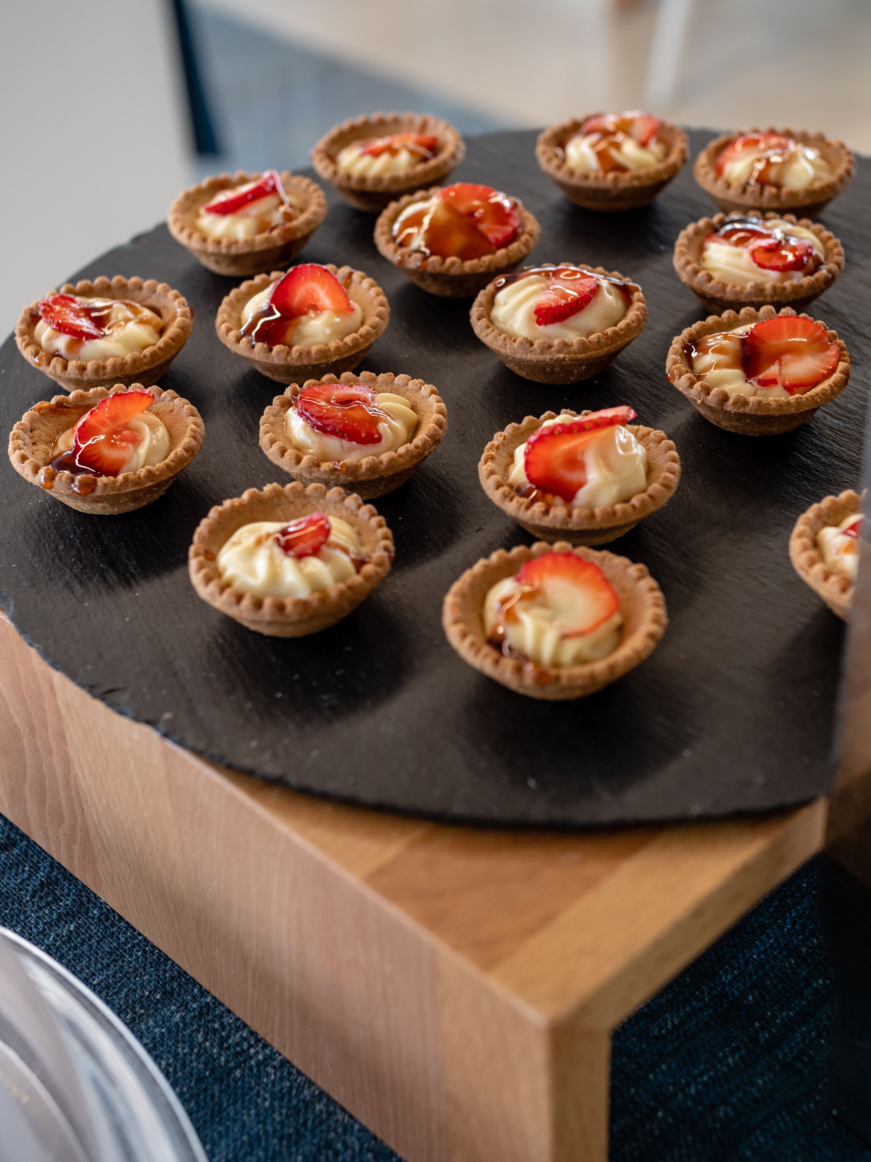 A slate serving board with mini tarts topped with strawberries and whipped cream.