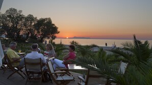 Un groupe de personnes est assis sur des chaises longues, face à un coucher de soleil sur l’eau.