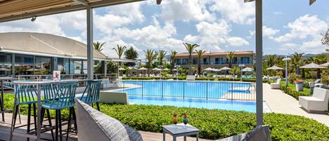 A poolside area with outdoor seating, a pool, and a building in the background.