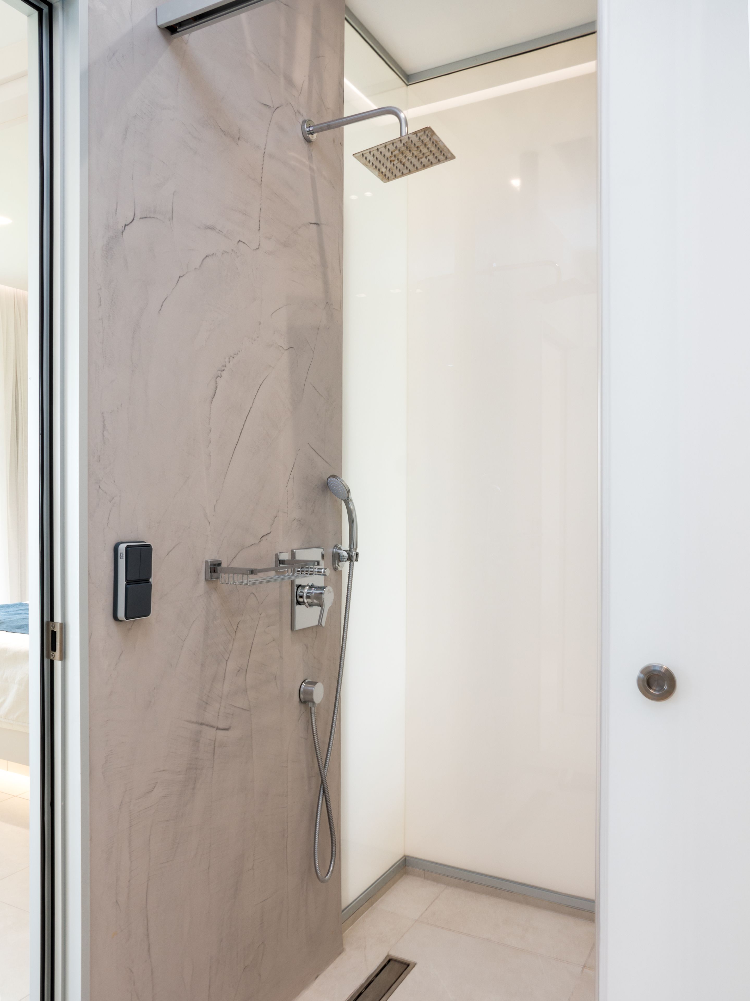 A modern bathroom with a glass shower enclosure, a handheld showerhead, and a wall-mounted control panel.
