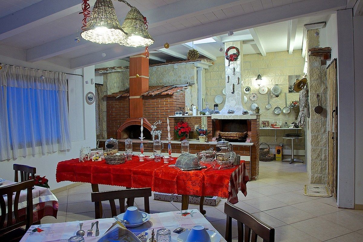 A dining area with a red tablecloth, wooden chairs, and a brick oven in the background.
