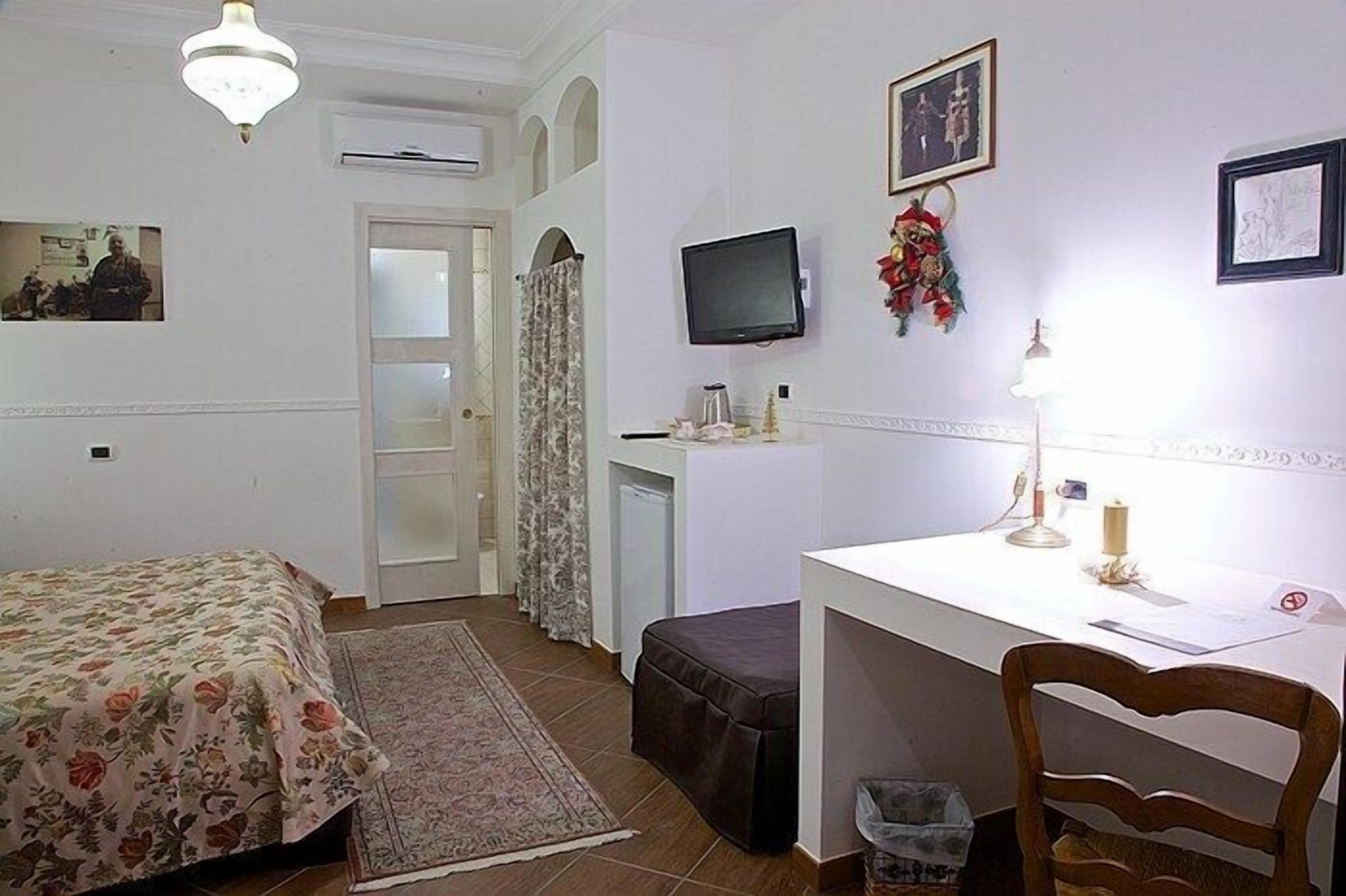 A bedroom with a bed, a desk, a chair, a television, and a small table with a lamp.