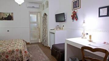 A bedroom with a bed, a desk, a chair, a television, and a small table with a lamp.