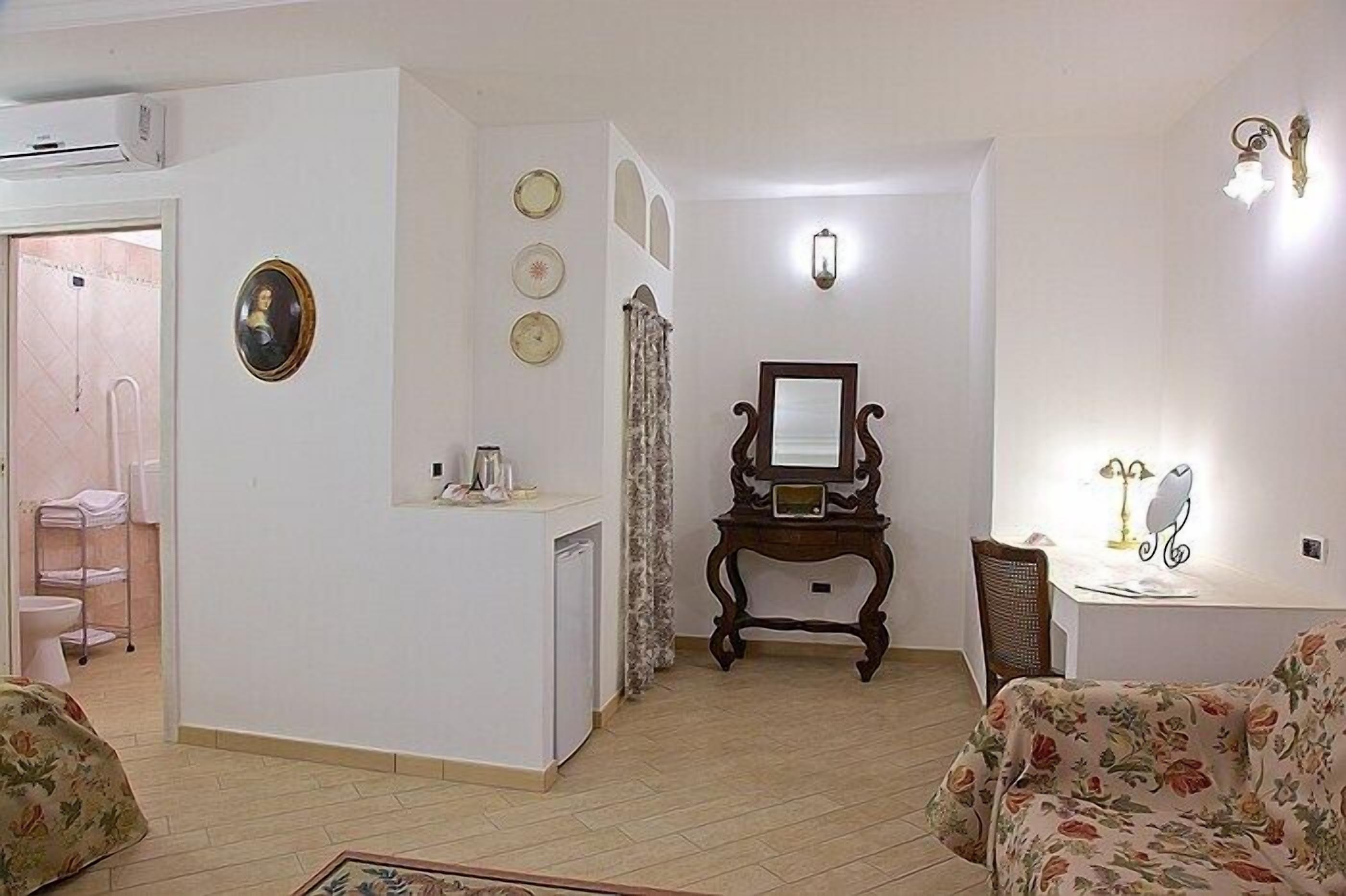 Una sala de estar con sofá, mesa de centro, mesita auxiliar con lámpara, espejo y un mueble bajo.