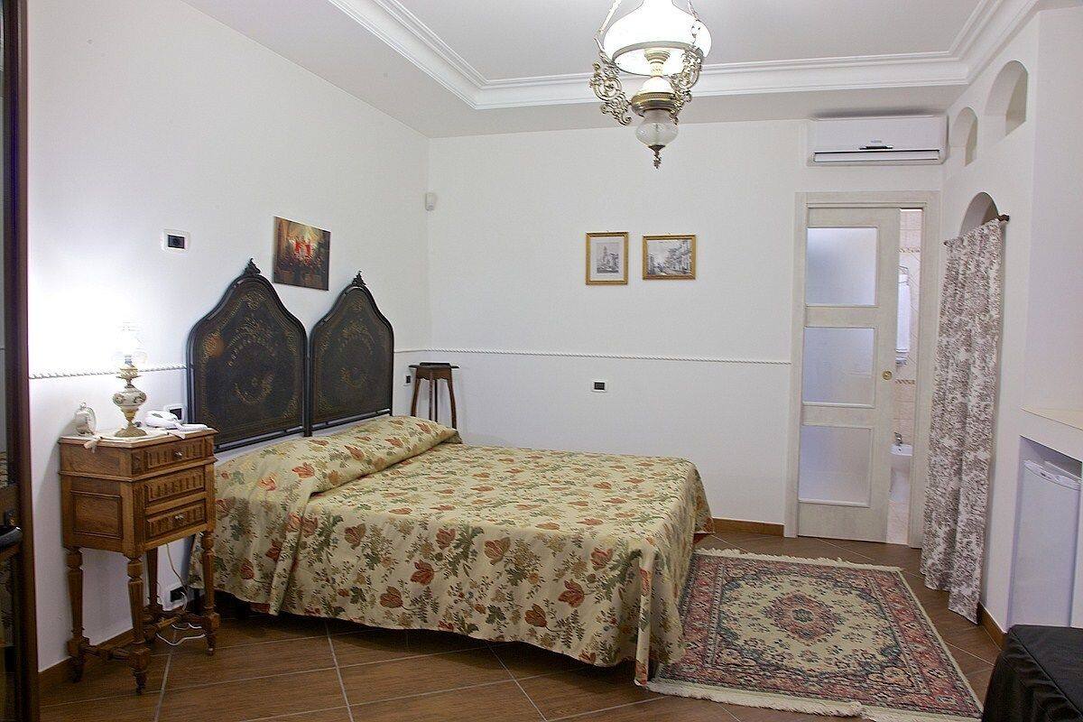 Un dormitorio con una cama, una mesita de noche, una lámpara, una alfombra y una puerta con cortina.