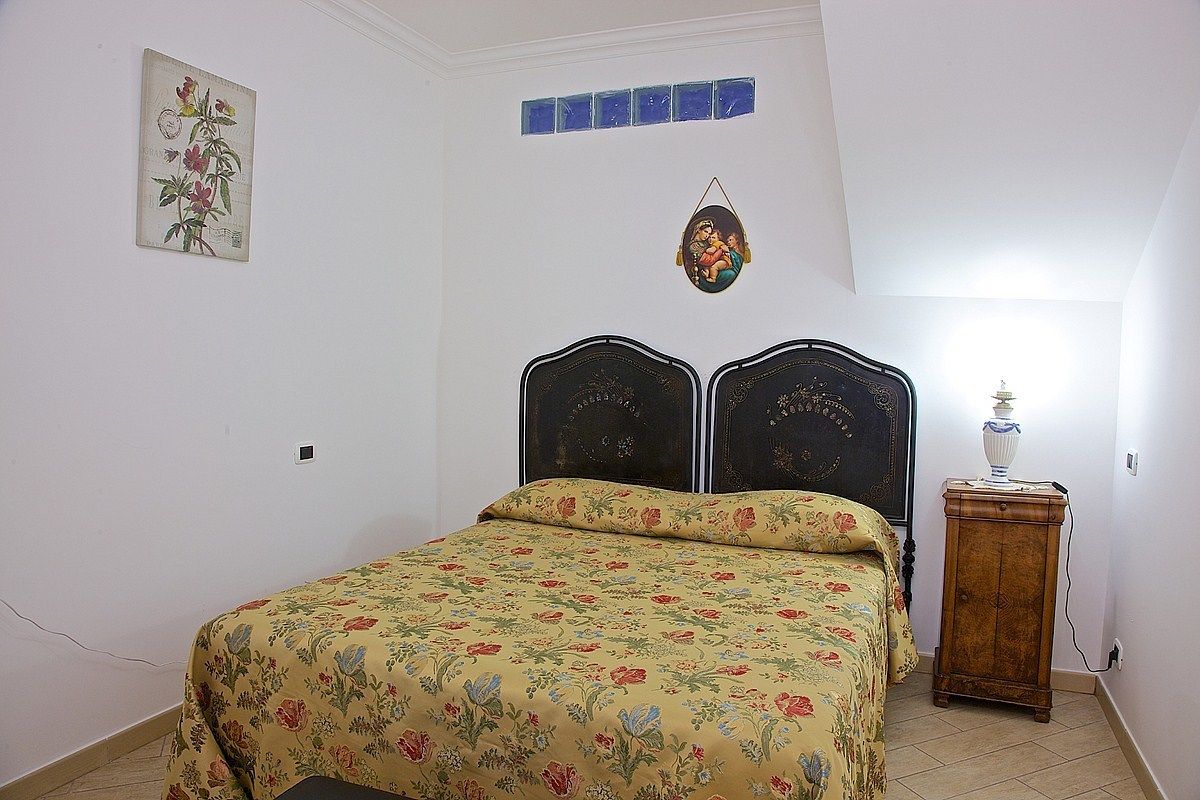 Une chambre à coucher avec une couvre-lit à motifs floraux, une table de chevet en bois avec une lampe et un tableau accroché au mur.