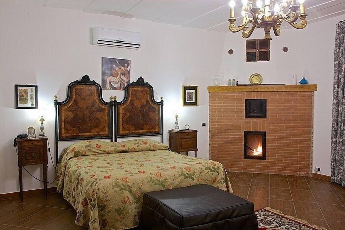 Un dormitorio con una cama doble, chimenea, candelabro y una mesita de noche con lámpara.