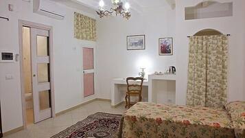 A bedroom with a bed, a desk, a chair, a radiator, and a door.