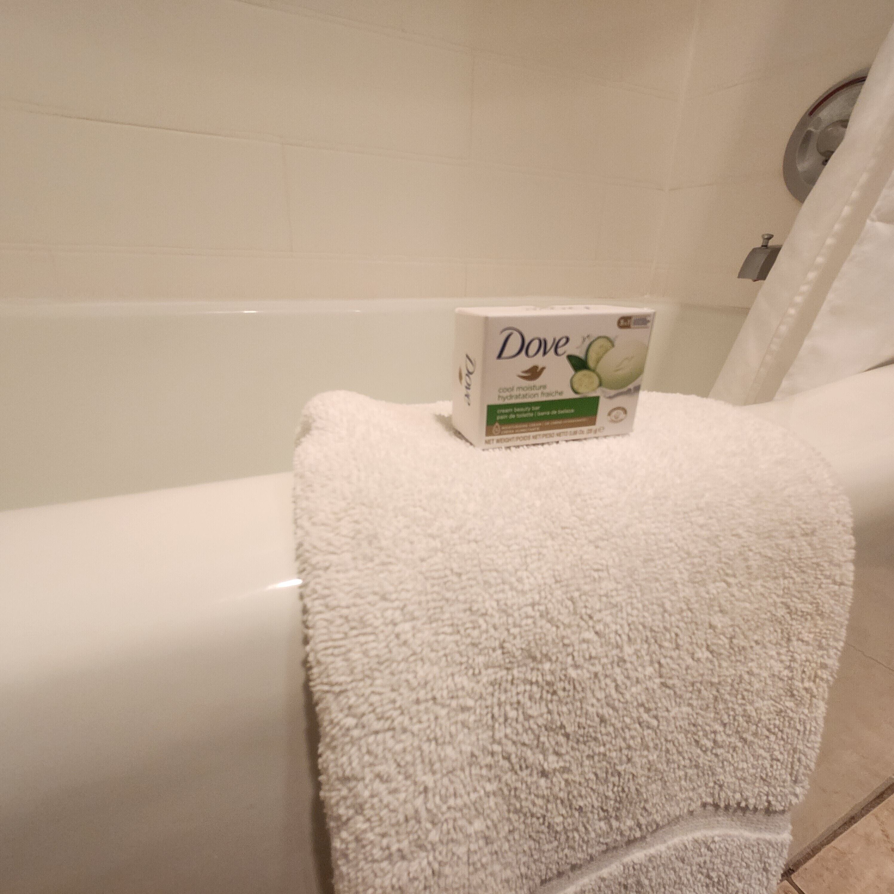 A white towel on a bathtub with a Dove moisturizing bar.