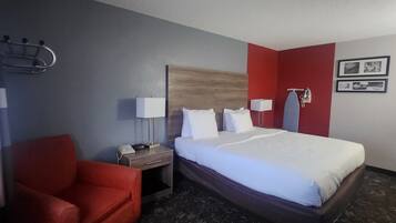 Una habitación de hotel con cama, un sillón rojo, una mesita de noche con lámpara y un teléfono instalado en la pared.